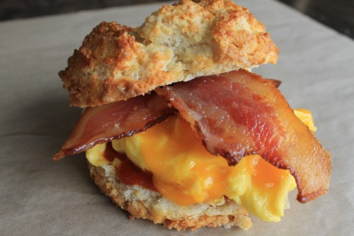 A biscuit sandwich filled with scrambled eggs, melted cheese, crispy bacon, and a drizzle of ketchup.