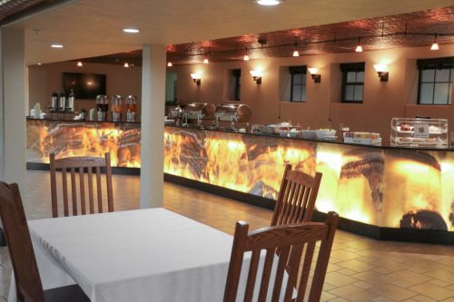 A cozy dining area with wooden chairs and a buffet counter featuring warm lighting and a decorative stone backdrop.