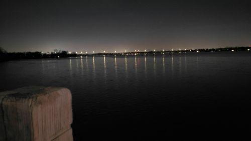 A calm river at night, reflecting lights from a distant bridge under a dark sky.