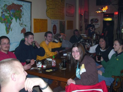 A group of friends enjoying drinks and snacks at a bar, smiling and chatting around a wooden table.