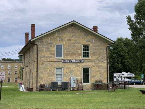 Historic stone building labeled "Mineral Point," surrounded by greenery and parked vehicles.