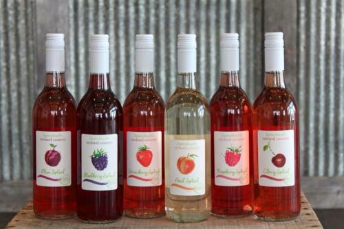 Seven bottles of fruit-flavored sodas lined up on a wooden surface, featuring colorful labels with fruit illustrations.