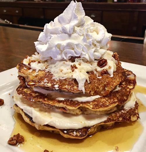 A stack of three pancakes topped with whipped cream, nuts, and syrup on a white plate.