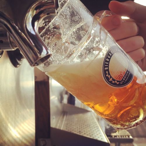 A hand pours a golden beer from a tap into a clear glass mug, with bubbles rising in the drink.
