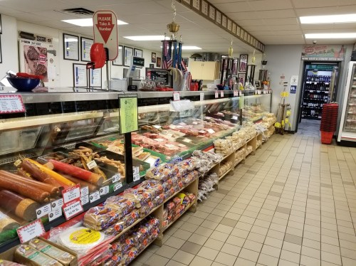 A deli display case filled with various meats, cheeses, and packaged goods in a well-lit store.