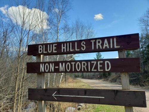Sign for Blue Hills Trail, indicating it's non-motorized, with a dirt path and trees in the background.