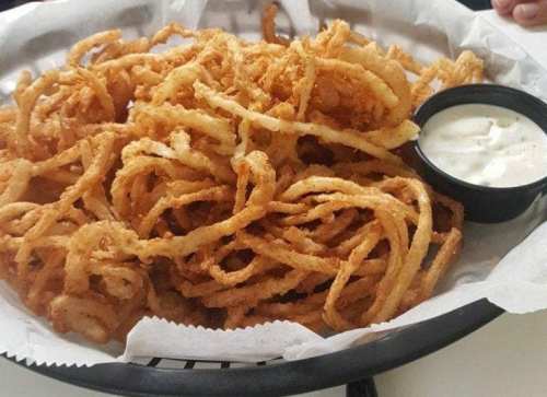 A basket of crispy, golden curly fries served with a small cup of dipping sauce.