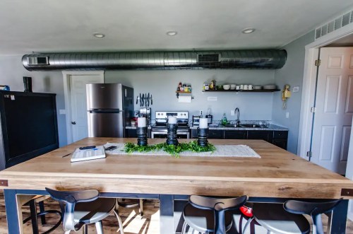 Modern kitchen with a large wooden table, stainless steel appliances, and a minimalist decor featuring greenery.