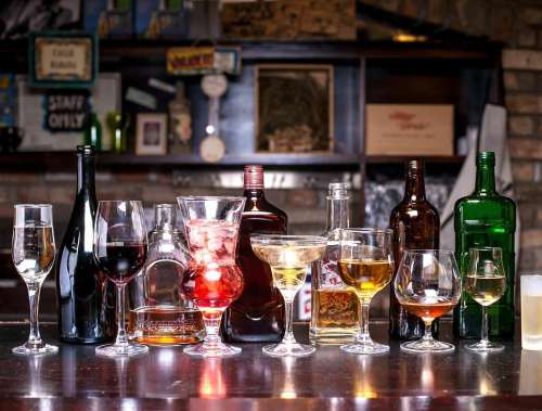 A variety of alcoholic beverages displayed on a bar, including wine, cocktails, and spirits in different glassware.