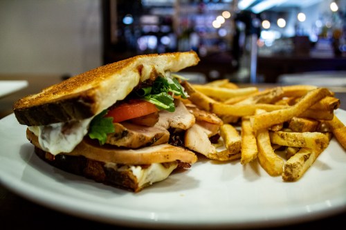 A toasted sandwich with turkey, lettuce, and tomato, served with a side of golden French fries on a white plate.