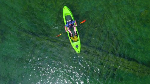 Aerial view of a person in a bright green kayak paddling on clear, calm water.