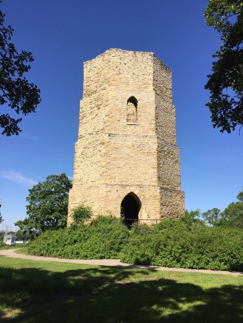 A tall, stone tower surrounded by greenery under a clear blue sky.