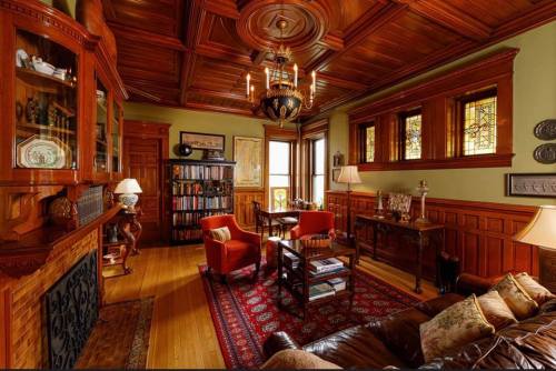 A cozy, vintage library with wooden paneling, a chandelier, bookshelves, and comfortable seating.