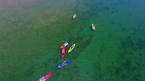 Aerial view of colorful kayaks on clear blue water, with paddlers enjoying a sunny day.