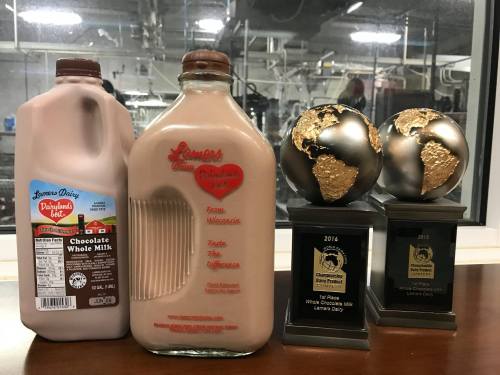 A bottle of chocolate whole milk next to two globe trophies and a third trophy, all on a wooden surface.