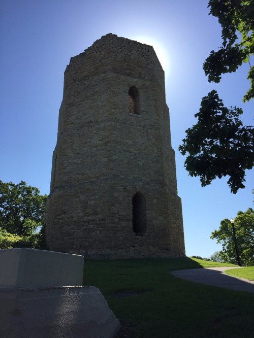 A tall stone tower silhouetted against a bright sky, surrounded by greenery.