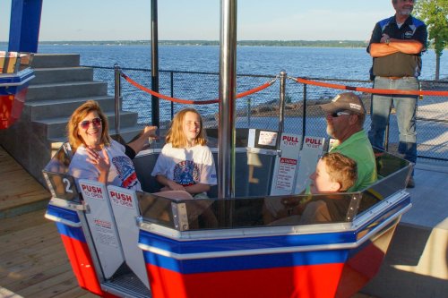 A family enjoys a ride on a spinning attraction by the water, smiling and laughing together.