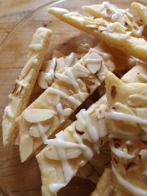 A close-up of almond-topped cookies drizzled with white icing on a wooden surface.
