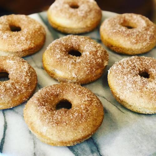 A plate of freshly baked donuts coated in cinnamon sugar, arranged neatly on a marble surface.