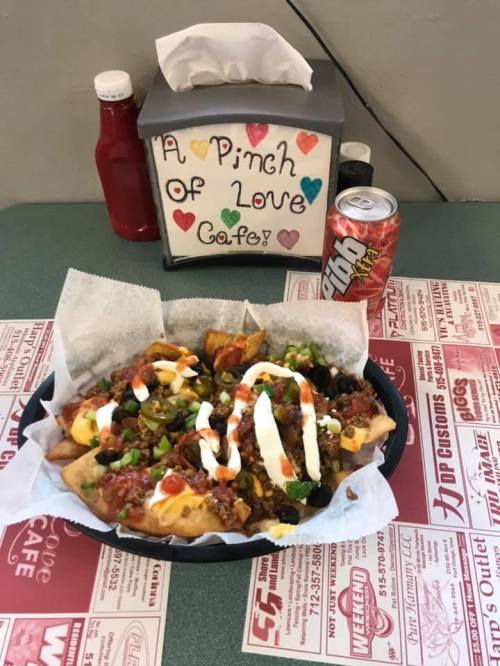 A plate of loaded nachos topped with salsa, sour cream, and various toppings, with a drink and condiments in the background.