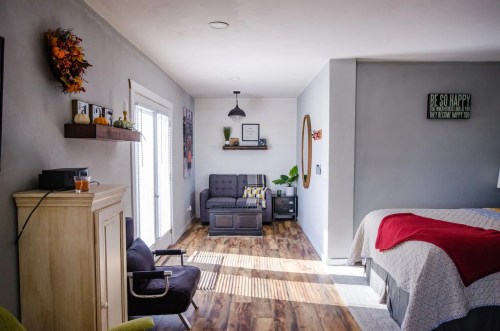 Cozy room featuring a bed, seating area, and natural light, with modern decor and wooden flooring.