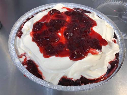 A pie with a creamy white topping and a layer of cherry filling on top, served in a silver aluminum pie dish.