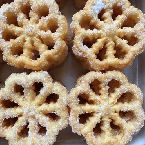 Four golden, flower-shaped sweets dusted with sugar, arranged neatly on a tray.