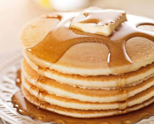 A stack of fluffy pancakes topped with a pat of butter and drizzled with syrup.