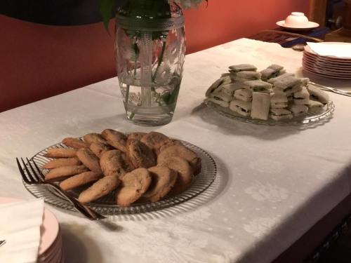 A table set with a platter of cookies and a plate of rolled sandwiches, with decorative items in the background.