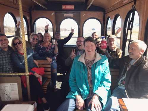 A group of people smiling and posing for a photo inside a trolley, with some making peace signs.