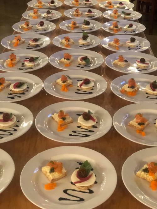 A long table set with numerous plates, each featuring a small appetizer garnished with colorful toppings.