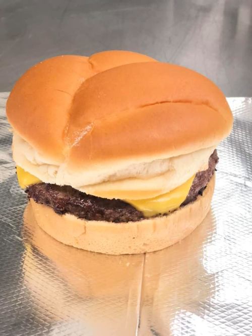 A cheeseburger with two soft buns, a juicy beef patty, and melted cheese, resting on a silver foil surface.