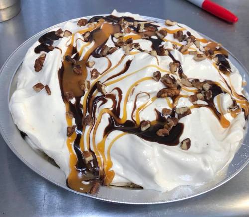 A creamy dessert topped with whipped cream, chocolate and caramel drizzle, and chopped nuts in a pie dish.