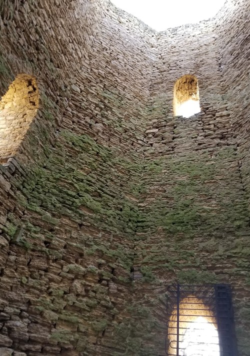Interior view of a stone structure with moss-covered walls and windows, illuminated by natural light from above.