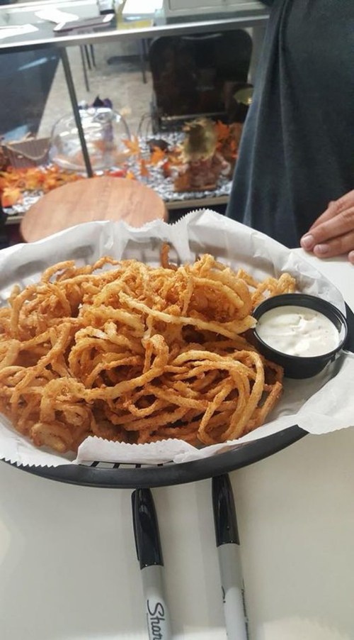 A basket of crispy, golden onion rings served with a small cup of dipping sauce.