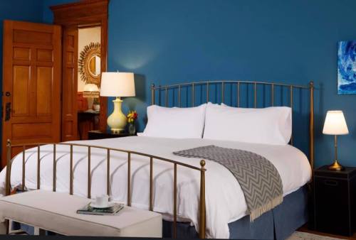 Cozy bedroom with a brass bed, blue walls, and warm lighting, featuring a nightstand and a small table with a cup.