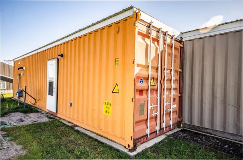 An orange shipping container converted into a small building, with a door and warning signs, set on grassy ground.