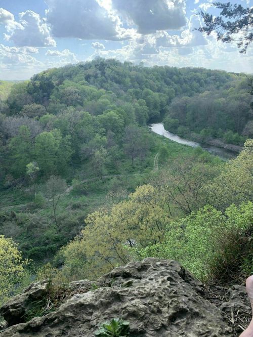 A scenic view of a lush green valley with a winding river, surrounded by hills and a partly cloudy sky.