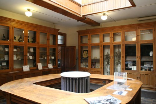 A wooden display area in a museum featuring glass cabinets with artifacts and a central circular table.