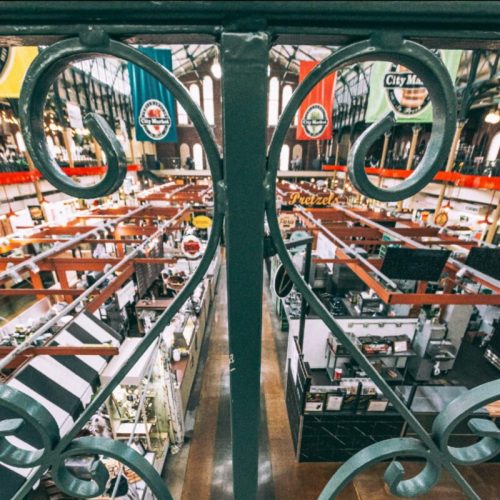 View from above of a bustling market with various stalls and colorful banners hanging from the ceiling.