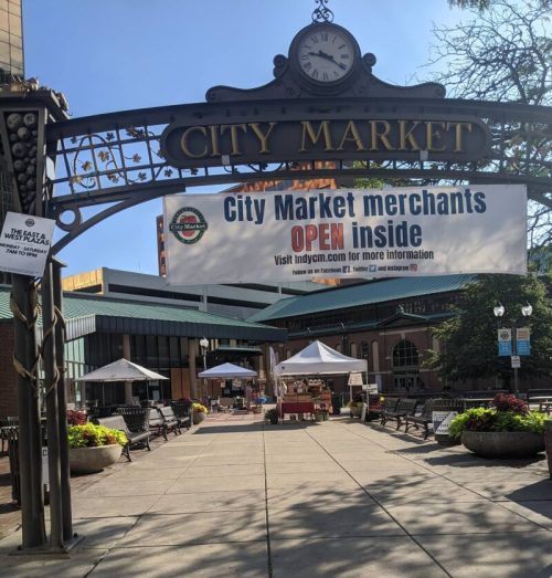 Entrance to City Market with a banner stating "City Market merchants OPEN inside" and tents set up for vendors.