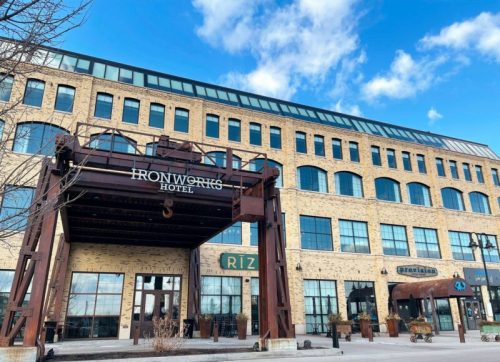 Exterior of Ironworks Hotel featuring a brick facade, large windows, and a metal entrance sign against a blue sky.