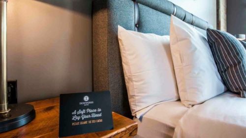 A cozy hotel bed with white pillows and a sign that reads, "A Soft Place to Lay Your Head."
