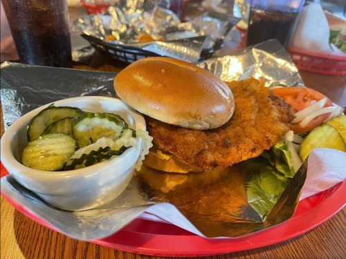 A crispy fried chicken sandwich on a bun, served with pickles and a side of coleslaw in a small bowl.