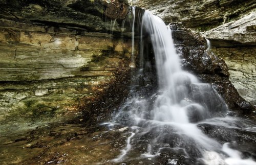 A serene waterfall cascading over rocky terrain, surrounded by textured stone walls and lush greenery.