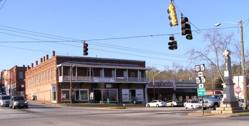 A street view of a small town intersection with a historic building, traffic lights, and a monument in the foreground.