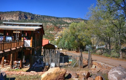 A rustic building with a wooden deck, surrounded by trees and mountains under a clear blue sky.