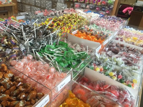 A colorful display of various candies in clear containers, including lollipops, gummies, and wrapped sweets.