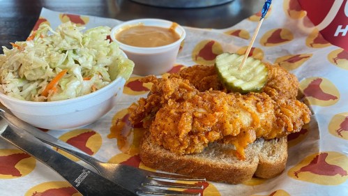 A plate featuring fried chicken strips on toast, a pickle slice, coleslaw, and a small cup of sauce.