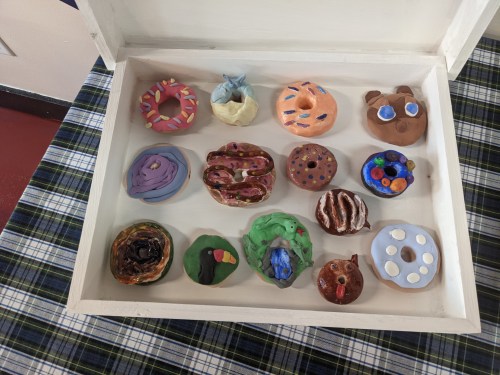A wooden box containing colorful, handmade clay donuts and pastries arranged in two rows.